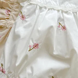 Detailed view of delicate pink cherry blossom embroidery and lace trim on baby cotton romper