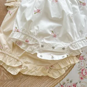 Close-up of cotton baby bodysuit with floral embroidery and metal snap buttons