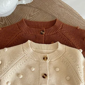 Detailed close-up of knitted pom-pom textures on brown and beige baby girl cardigans