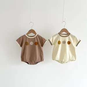 Detail of two cotton baby bodysuits in brown and cream colors with smiling flower prints