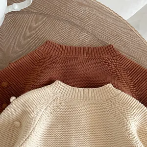 Detail of chunky knit sweaters in caramel and cream with textured bobble decorations