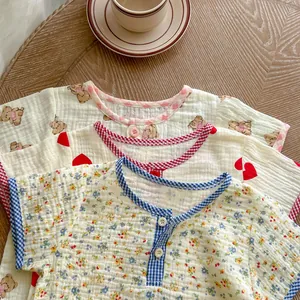 Close-up of cotton gauze baby t-shirts featuring bear and heart prints on a wood table