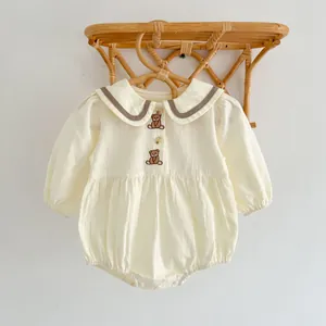Gros plan d'une barboteuse crème pour bébé avec broderie ours et boutons en bois sur blanc
