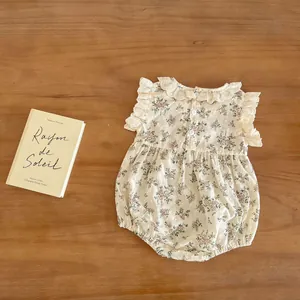 Detail view of cotton floral baby romper featuring lace collar and flutter sleeves on wood