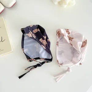 Detail of infant swim caps with chin straps and cute brown bear prints in pink and navy