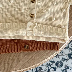 Detail of baby girl knitted cardigan with 3D pompom texture and ribbed cuffs