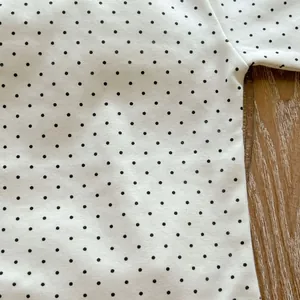Close-up of neat stitching and black polka dot pattern on soft white cotton baby romper