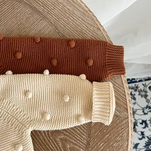 Detail of hand-knit girls cardigan with popcorn stitch balls and ribbed cuffs on wood table