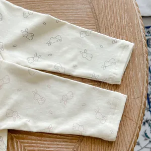 Close-up of cotton baby bodysuit cuffs with minimalist rabbit prints on cream fabric