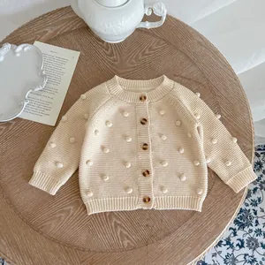 Detail of cream knit cardigan with handmade pom-poms and textured buttons on wood
