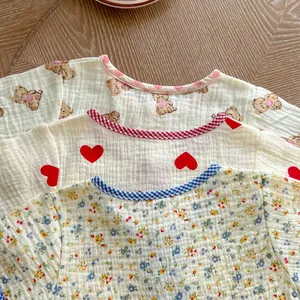 Detailed view of baby cotton gauze t-shirts with bear and heart prints on wood background