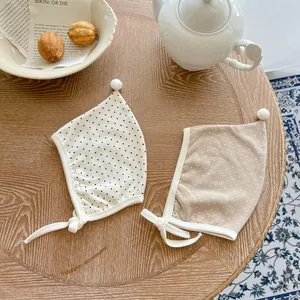 Two polka dot baby earflap hats with pom-poms on a wooden table for infant newborns