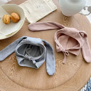 Close-up of baby knitted rabbit ear hats in grey and pink with chin straps on wooden table
