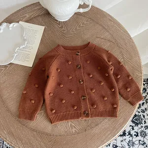 Detailed close-up of caramel knit cardigan with decorative pom-poms and wood buttons