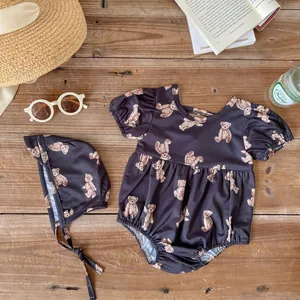 Flat lay of brown baby swimsuit with bear print and matching sun hat on wood