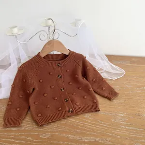 Close-up of caramel knit cardigan featuring decorative pom-poms and wood-textured buttons