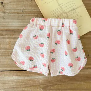 Dettaglio dei pantaloncini estivi per neonati in cotone con stampa fragola e quadretti
