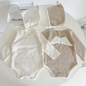 Detailed view of polka dot baby rompers with detachable angel wings on a flat lay