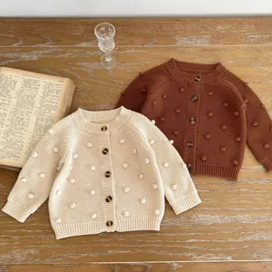 Detailed knit texture of girl's cardigans in cream and caramel with handmade pom-poms