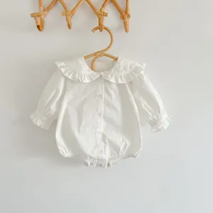 Détail d'un body blanc pour bébé avec col à volants et boutons sur un cintre rustique