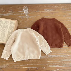 Flat lay of cream and caramel knit cardigans for girls with 3D pom-pom sleeves on wood