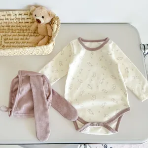 Detail of baby bunny print cotton romper and matching long-eared hat set on flat lay
