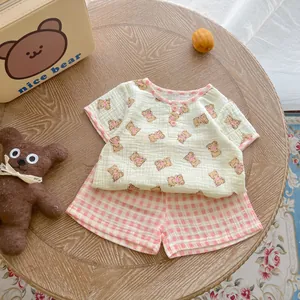 Flat lay of cotton infant summer set with bear print top and checkered shorts