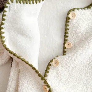 Detail of warm white fleece baby romper with green crochet edges and wooden buttons