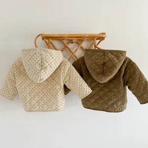 Detail of polka dot quilted baby jackets in beige and olive on a rattan hanger