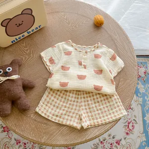 Detail of baby summer cotton set featuring bear print tee and plaid shorts on wood