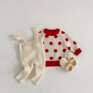 Detail of infant knit set with red polka dot sweater, beige overalls, and matching soft shoes