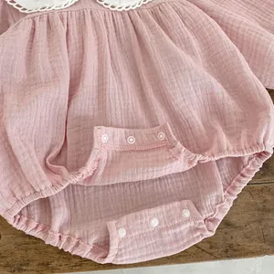 Pink cotton gauze baby bodysuit with lace collar and snap buttons on wooden background