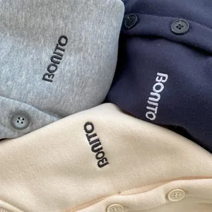 Detail of embroidered letters and buttons on fleece sweatshirts in gray, navy and beige