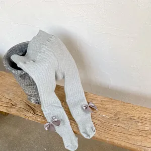 Detailed view of light gray ribbed knit baby leggings with a purple silk bow accent