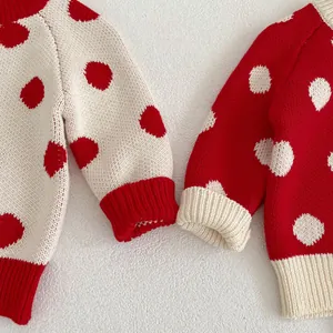 Detail of chunky knit baby sweaters with red and cream polka dots and ribbed cuffs