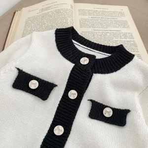 Detail der Baby-Strickjacke mit kontrastierendem schwarzem Besatz und verzierten Schleifenknöpfen