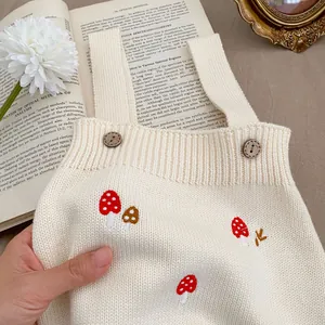 Infant cream knit romper featuring mushroom embroidery and wooden buttons on top of a book
