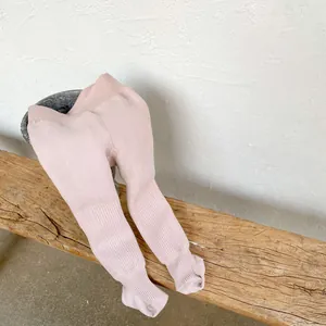 Close-up of light pink ribbed infant leggings on a rustic wooden bench background