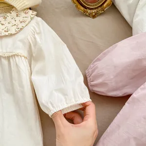 Gros plan des poignets élastiques et du col Claudine fleuri sur la barboteuse bébé