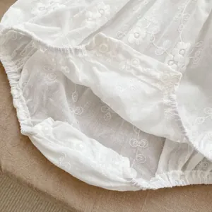 Close-up of white baby bodysuit featuring floral embroidery and snap buttons at the crotch