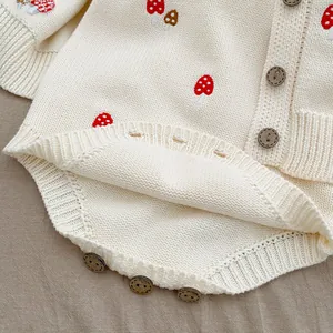 Detailed close-up of baby knit romper with mushroom embroidery and wooden buttons