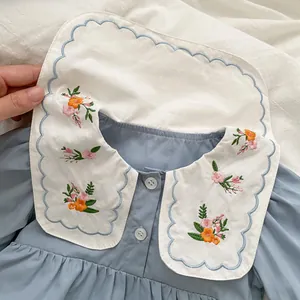 Close-up of floral embroidery on double-layered white collar of a light blue baby bodysuit