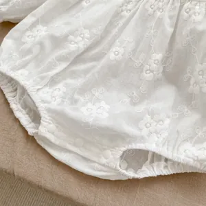 Detail of white cotton baby bodysuit showing floral embroidery and bottom snap buttons