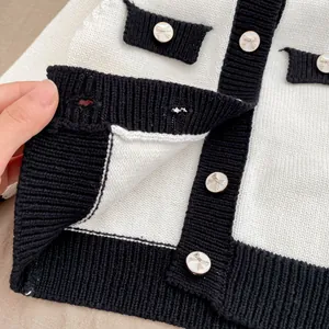 Detailaufnahme der Strickjacke mit schwarzer Kante und goldenen Schleifenknöpfen