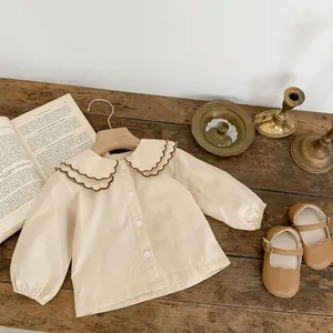 Detail eines Babyhemdes mit Wellensaumkragen und braunen Mary Jane Schuhen im Vintage-Stil