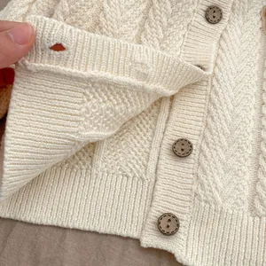 Nahaufnahme der cremefarbenen Strickjacke mit Zopfmustern und braunen Holzknöpfen im Detail