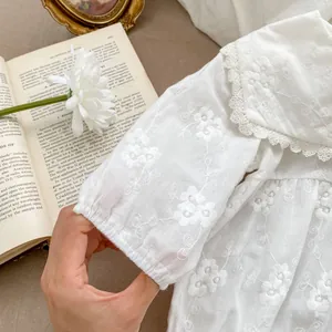 Close-up of white baby bodysuit with floral embroidery and delicate lace trim details