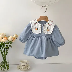 Close-up of white baby collar with floral embroidery and scalloped edges on blue bodysuit