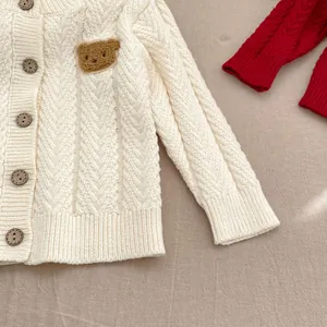 Detail der cremefarbenen Baby-Strickjacke mit Bären-Aufnäher und braunen Holzknöpfen