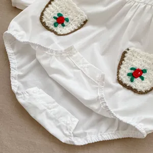 Detail of white cotton baby bodysuit showing crochet pockets with red flower embroidery